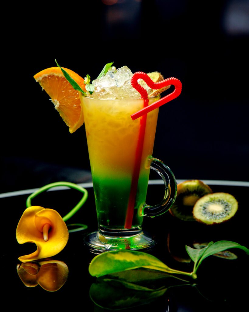 a glass of kiwifruit and orange cocktail garnished with orange and kiwifruit slice